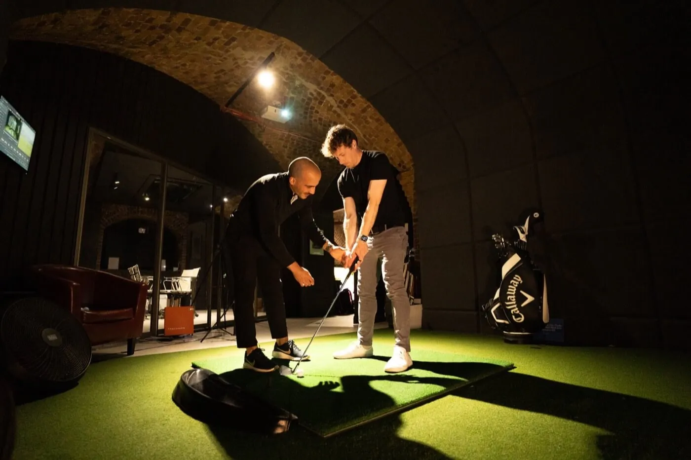 A professional coach giving a golf lesson in a Trackman bay at Grip Golf